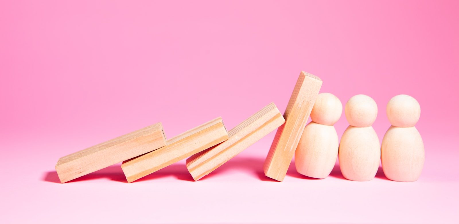 Wooden blocks falling towards small figures on pink background